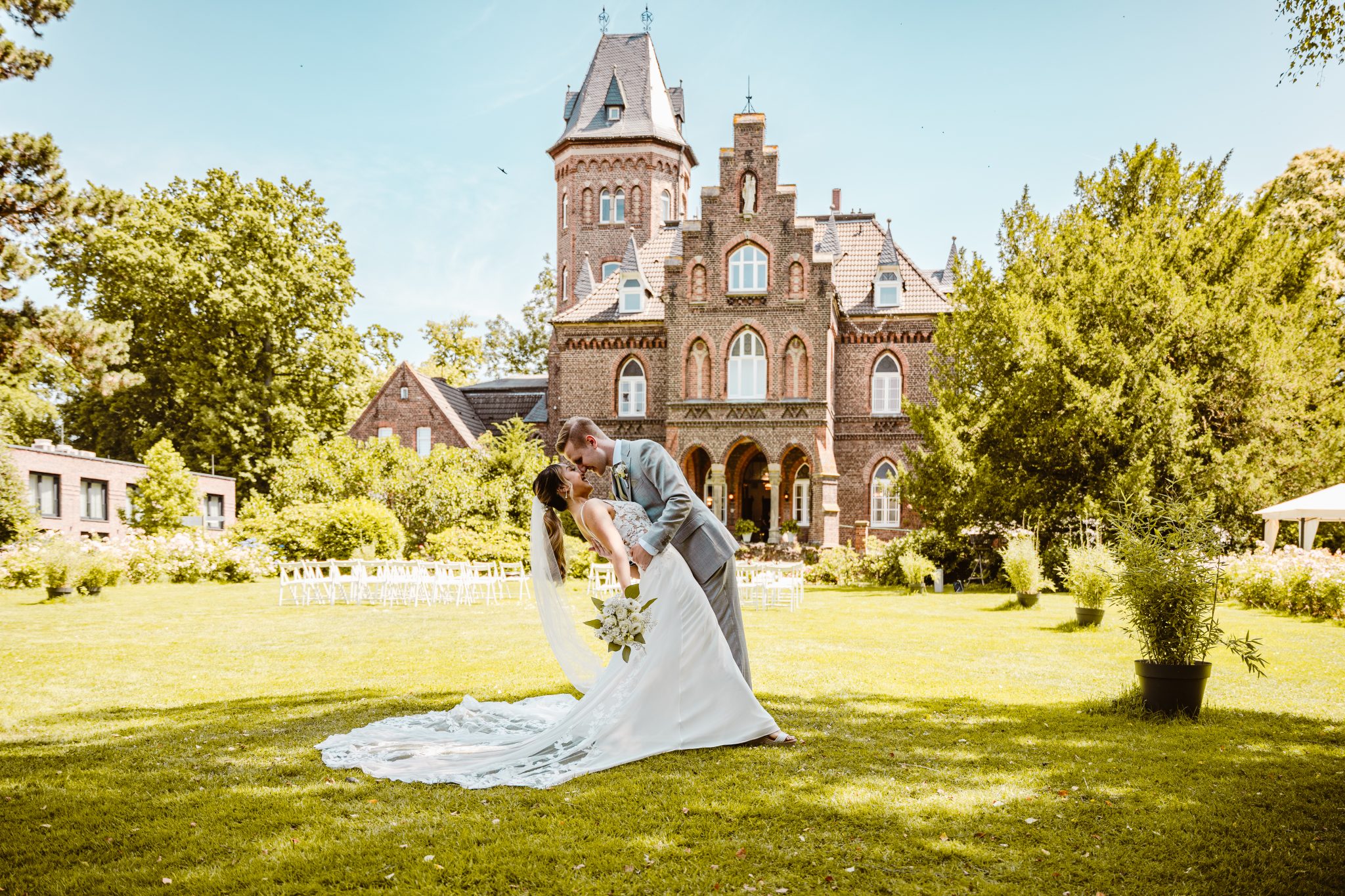 Ein Brautpaar steht draußen vor einem Backstein Schloss und küsst sich dramatisch
