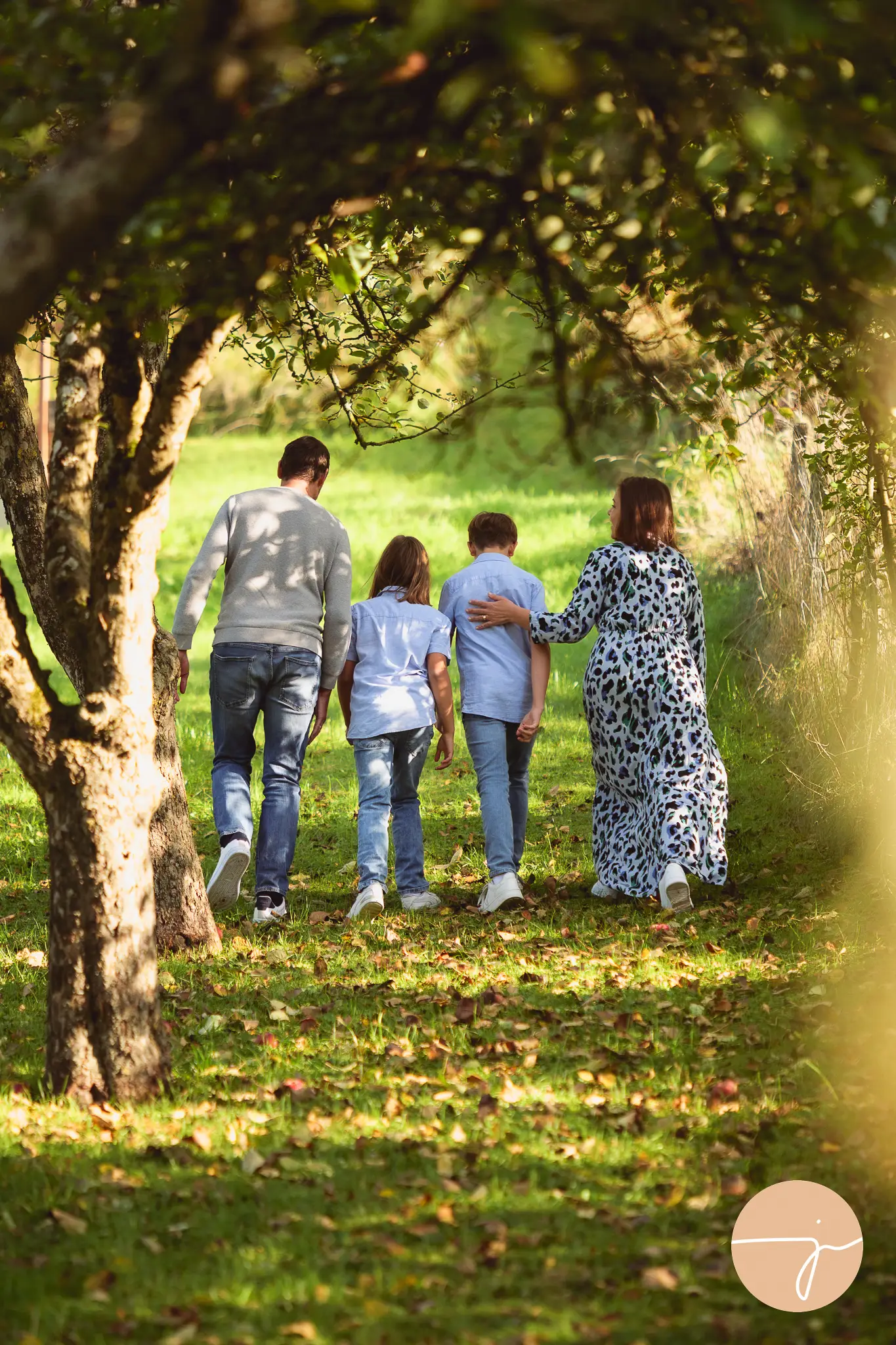 Eine Familie mit zwei Söhnen läuft in einer Allee zwischen Bäumen in der Natur. Wir sehen sie von hinten