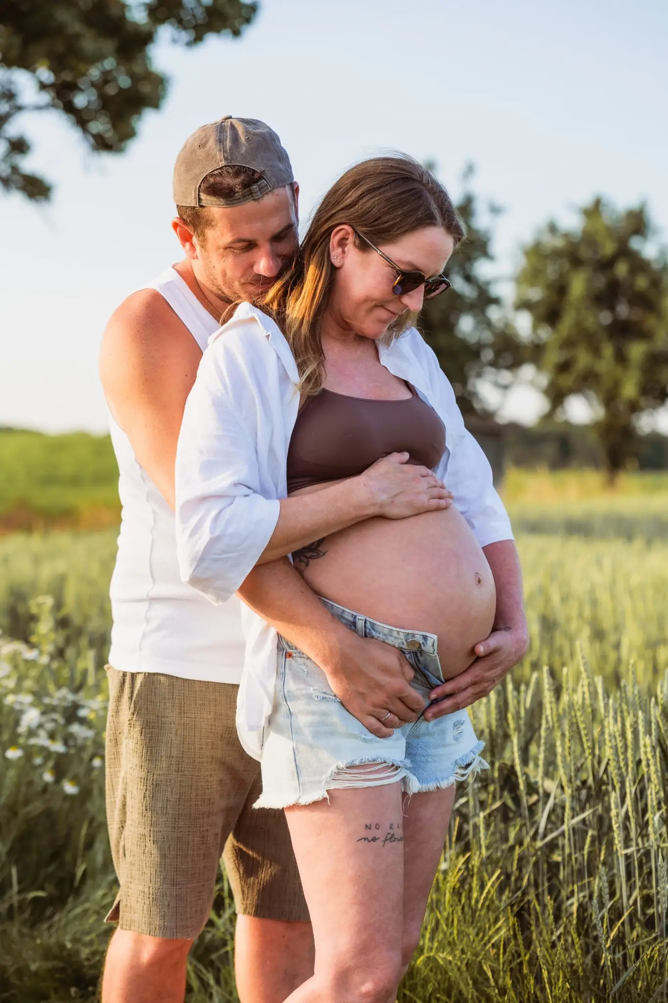 Schwangeres Pärchen schaut freudig auf ihren Babybauch während sie in einem Feld stehen