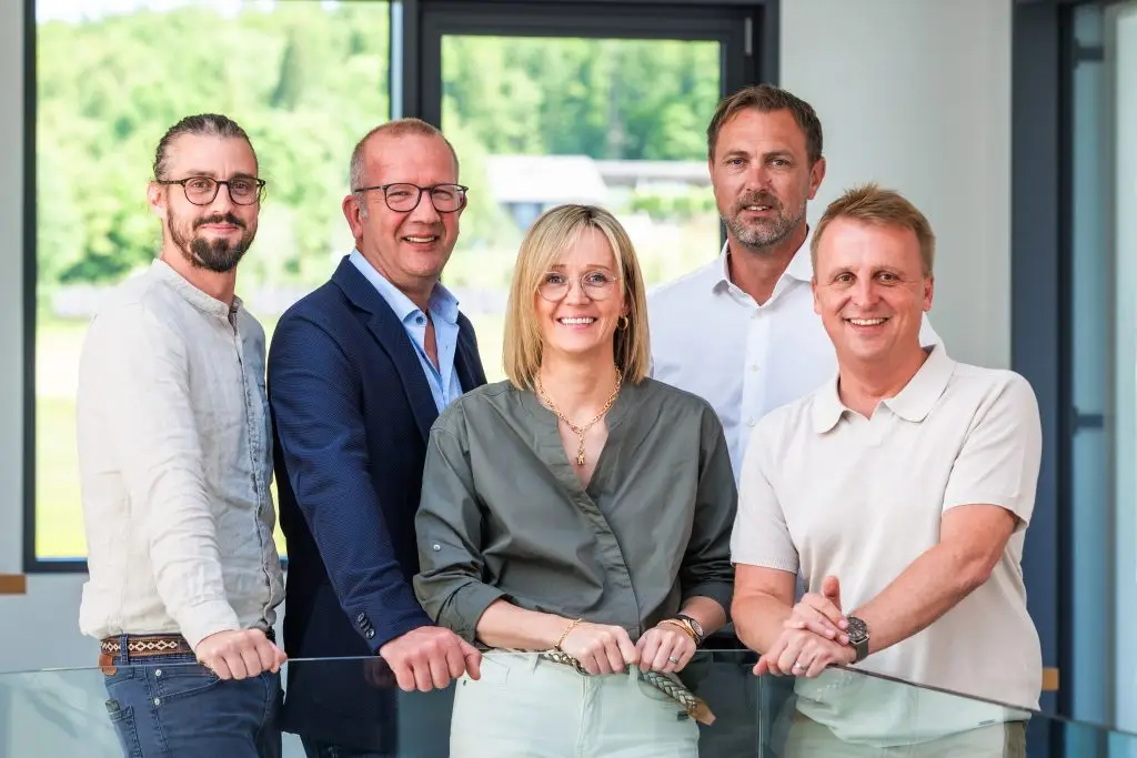 Ein Team von Geschäftsführern, die Geschäftsführerin in der Mitte. Alle lächeln freundlich in die Kamera.