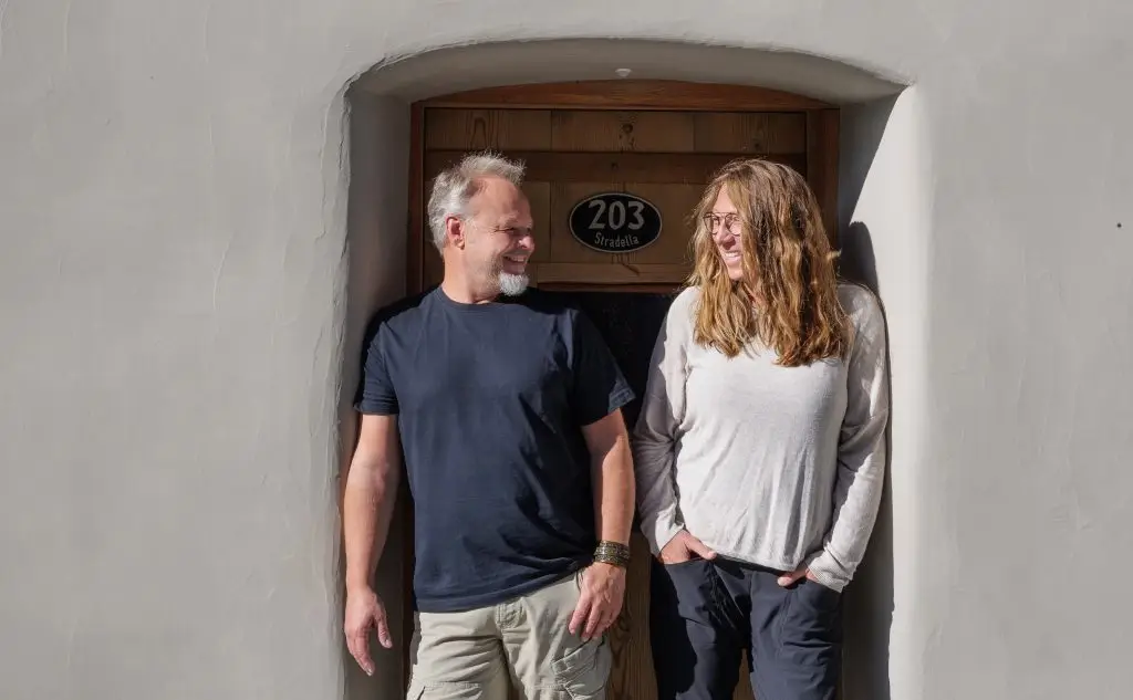 Die zwei Geschäftsführer von MAVAL Immobilien GmbH stehen in einem Hauseingang und lächeln sich gegenseitig an.