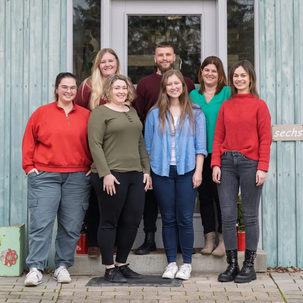 Ein Team von sieben Logopäd:innen vor einem blau-grünem Gebäude.