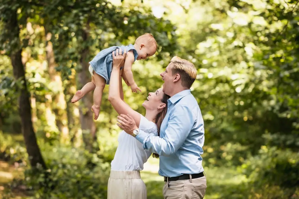Eine Frau hält lächelnd ihr Baby in die Luft, ihr Mann steht hinter ihr und grinst mit dem Baby um die Wette